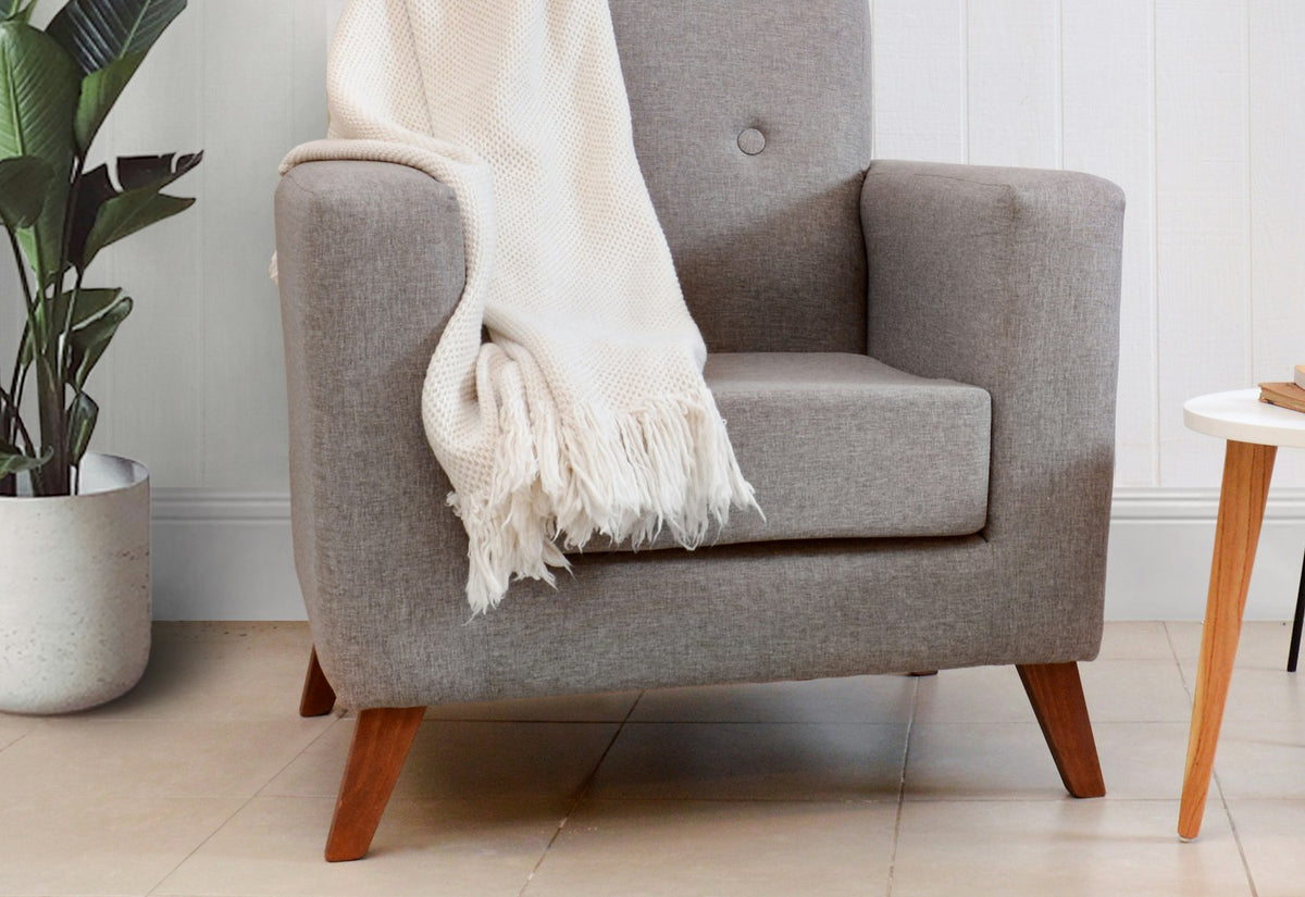 Cream fringed knit throw draped over a neutral armchair