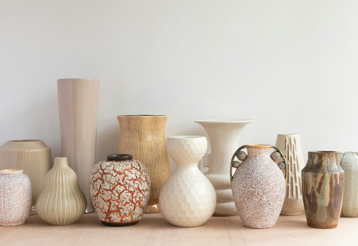 A row of ceramic vases in cream, sand and terracotta tones on pale wood